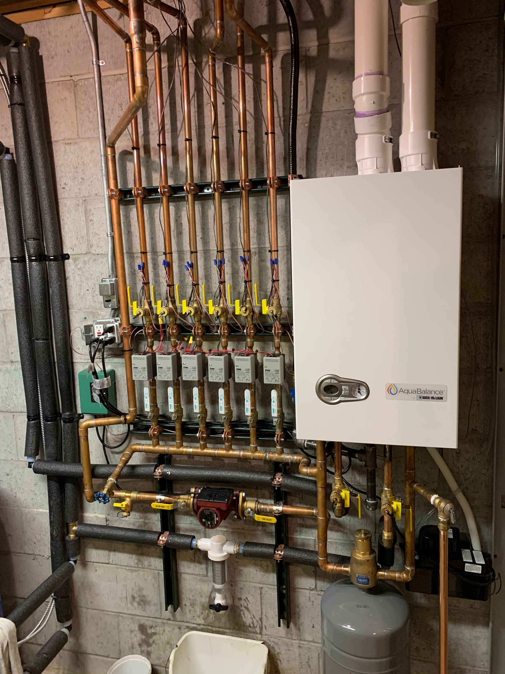 A boiler is installed in a basement with copper pipes.