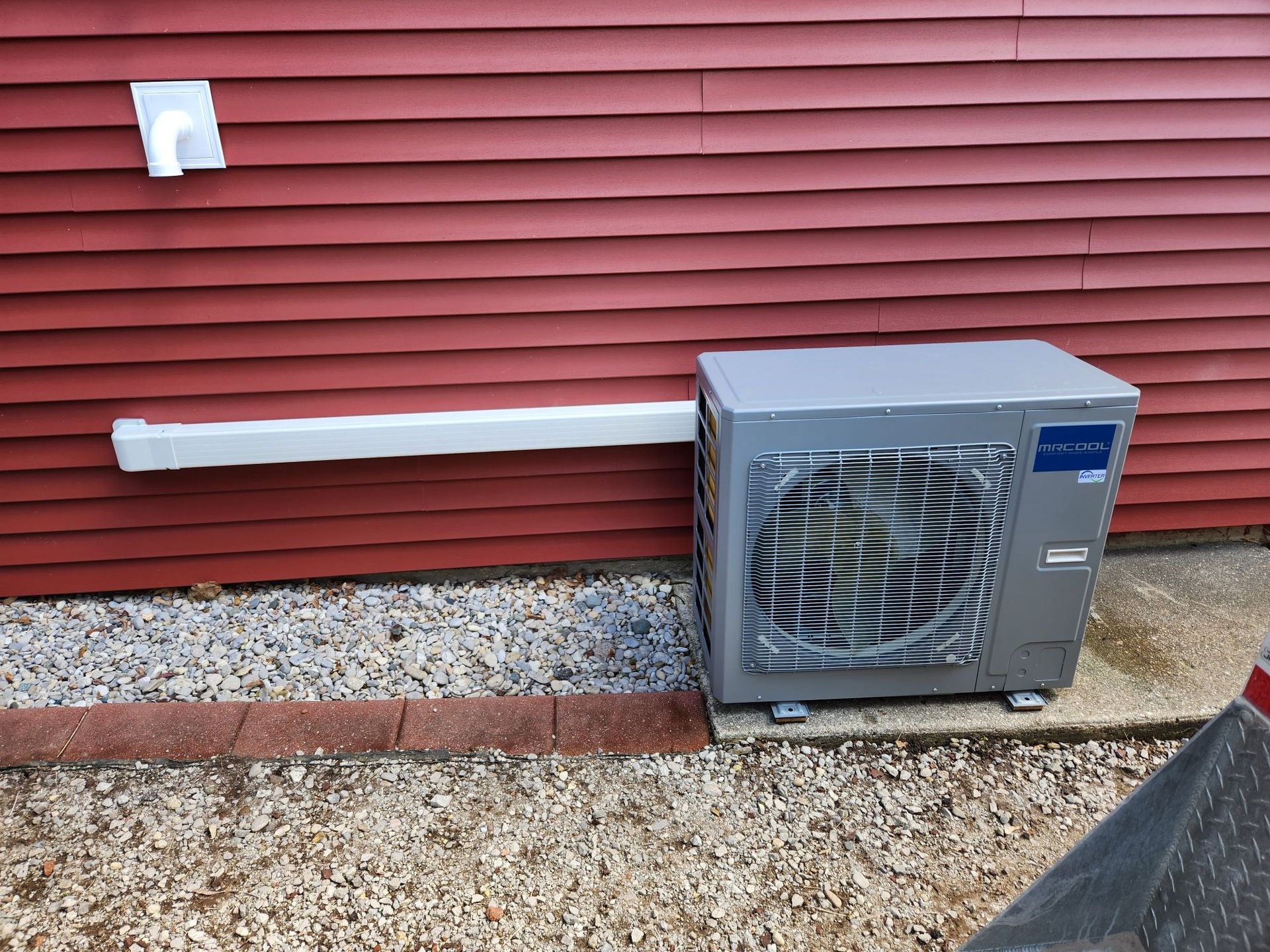 A gray air conditioner is sitting on the side of a red house.