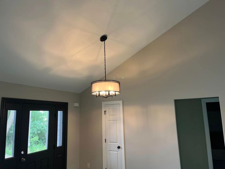 Dining room with a hanging light, white door, and black front doors in a beige interior.