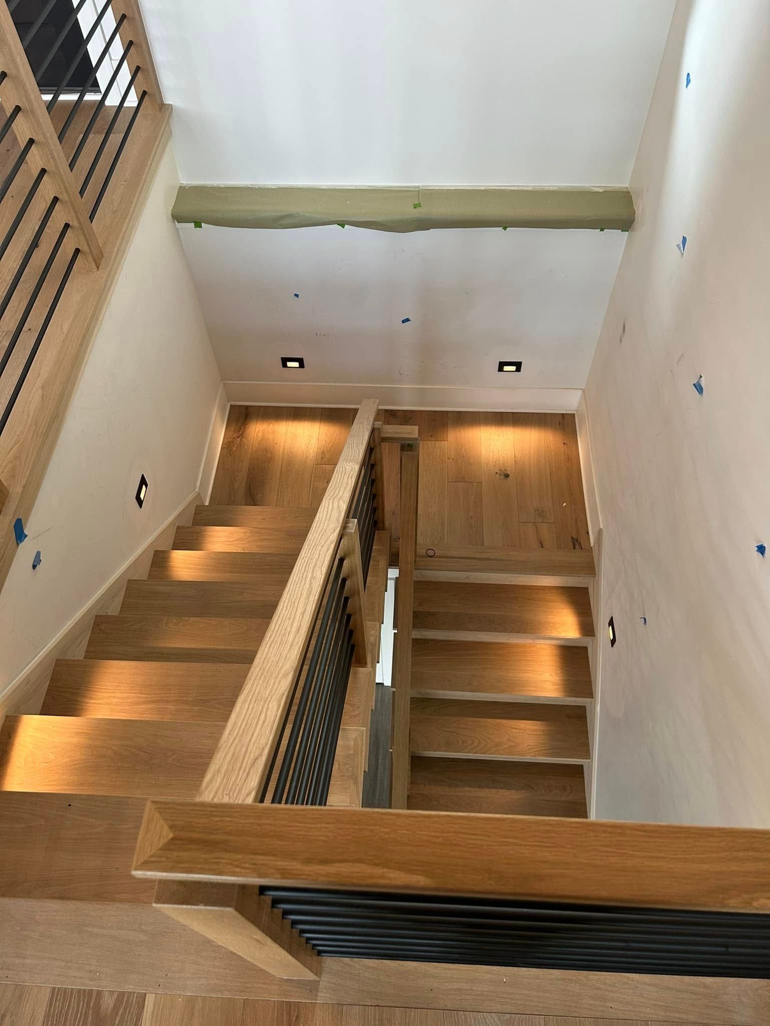 Modern stairwell with wooden steps, white walls, and railings viewed from above.