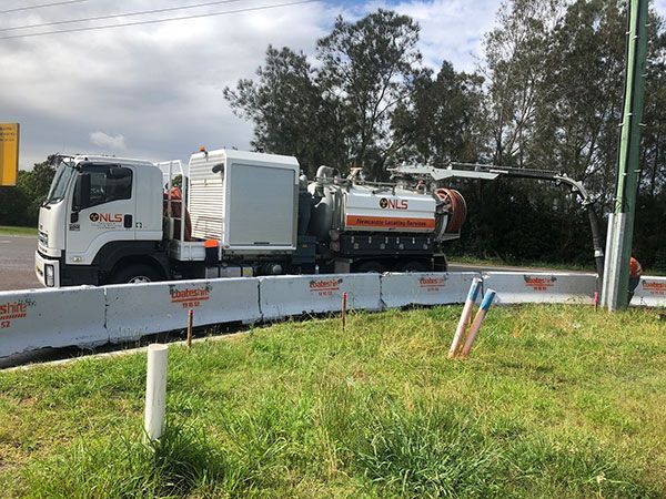 A vacuum truck is parked on the side of the road next to a grassy field.