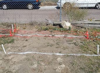A white car is parked in a parking lot next to a chain link fence.
