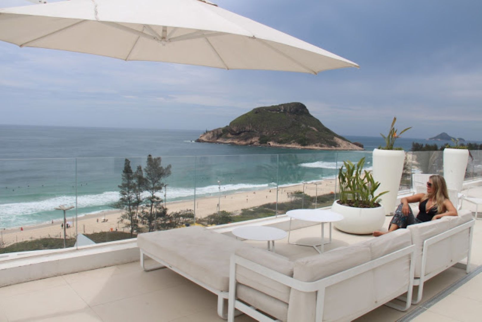 Uma mulher está sentada em um sofá na varanda com vista para o oceano.