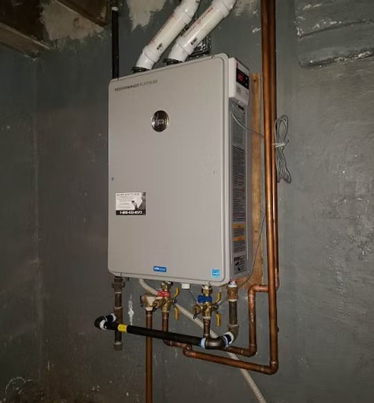A wall-mounted gray tankless water heater with white PVC venting pipes and copper plumbing against a gray concrete wall.