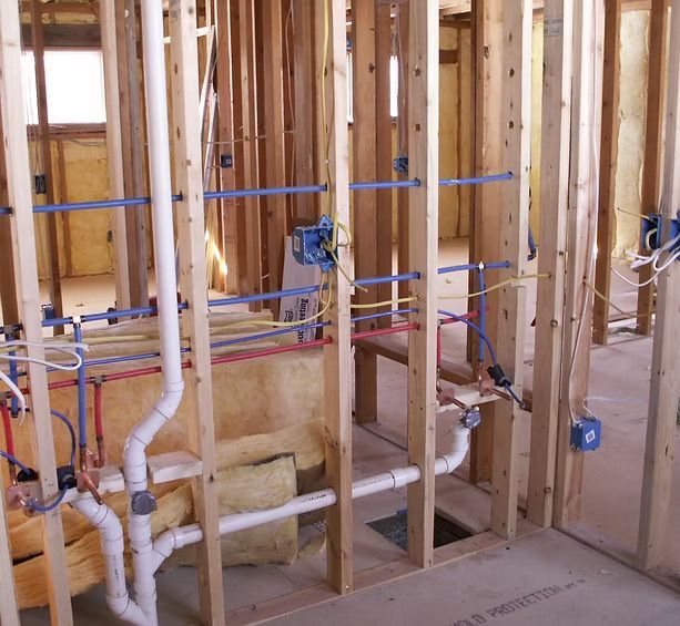 Unfinished interior wall frame showing exposed electrical wiring, blue PEX water lines, and white PVC plumbing pipes.