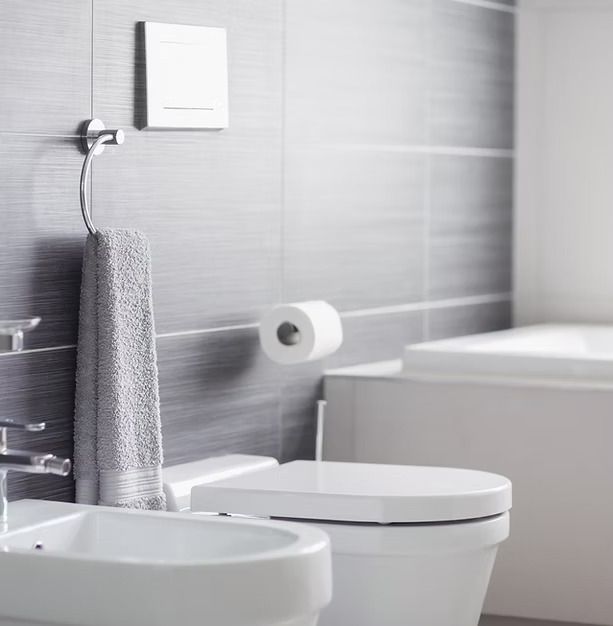 Modern bathroom with white bidet, toilet, grey tiled walls, and a gray hand towel on a ring.