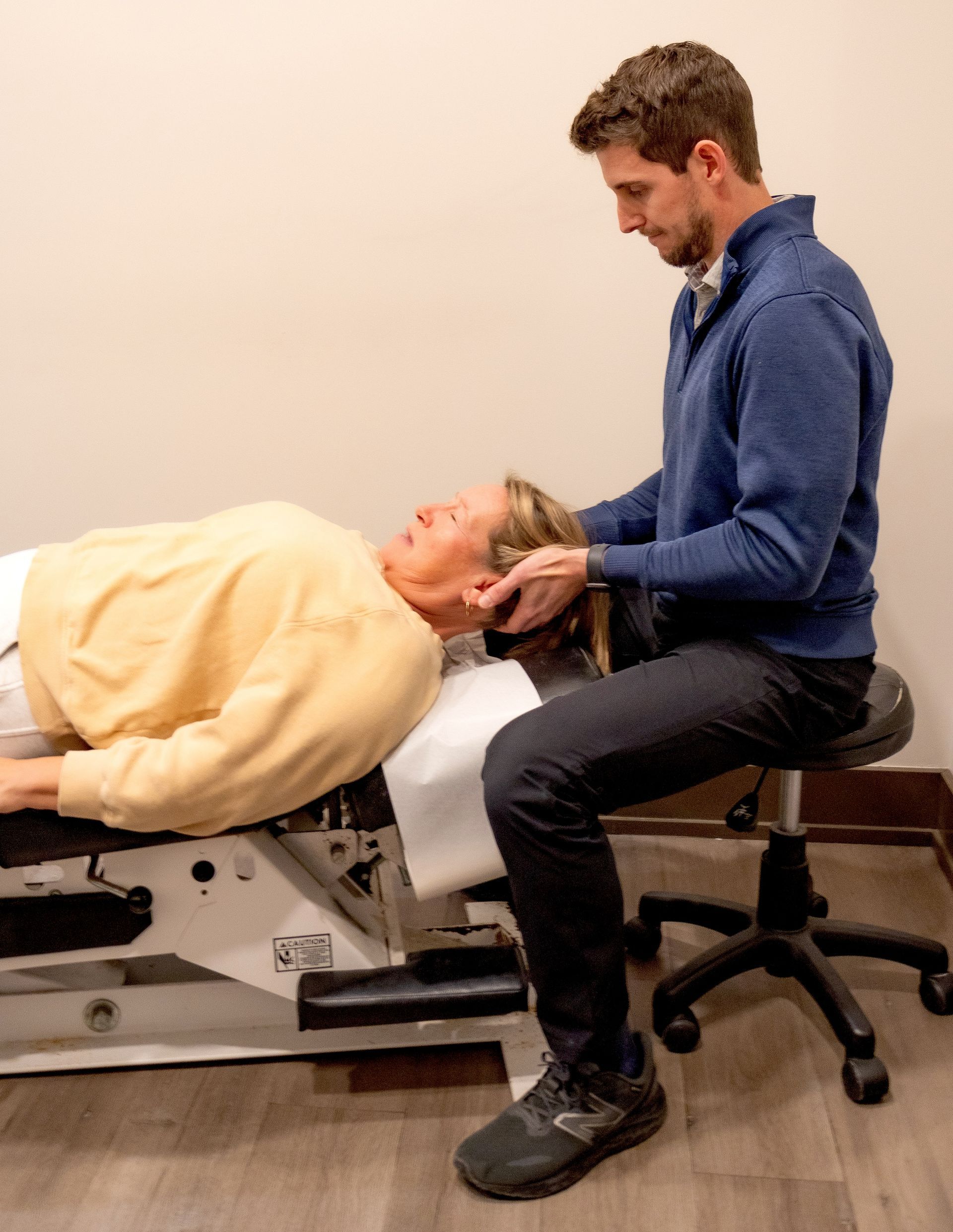 A man is sitting on a stool while a woman is laying on a table.