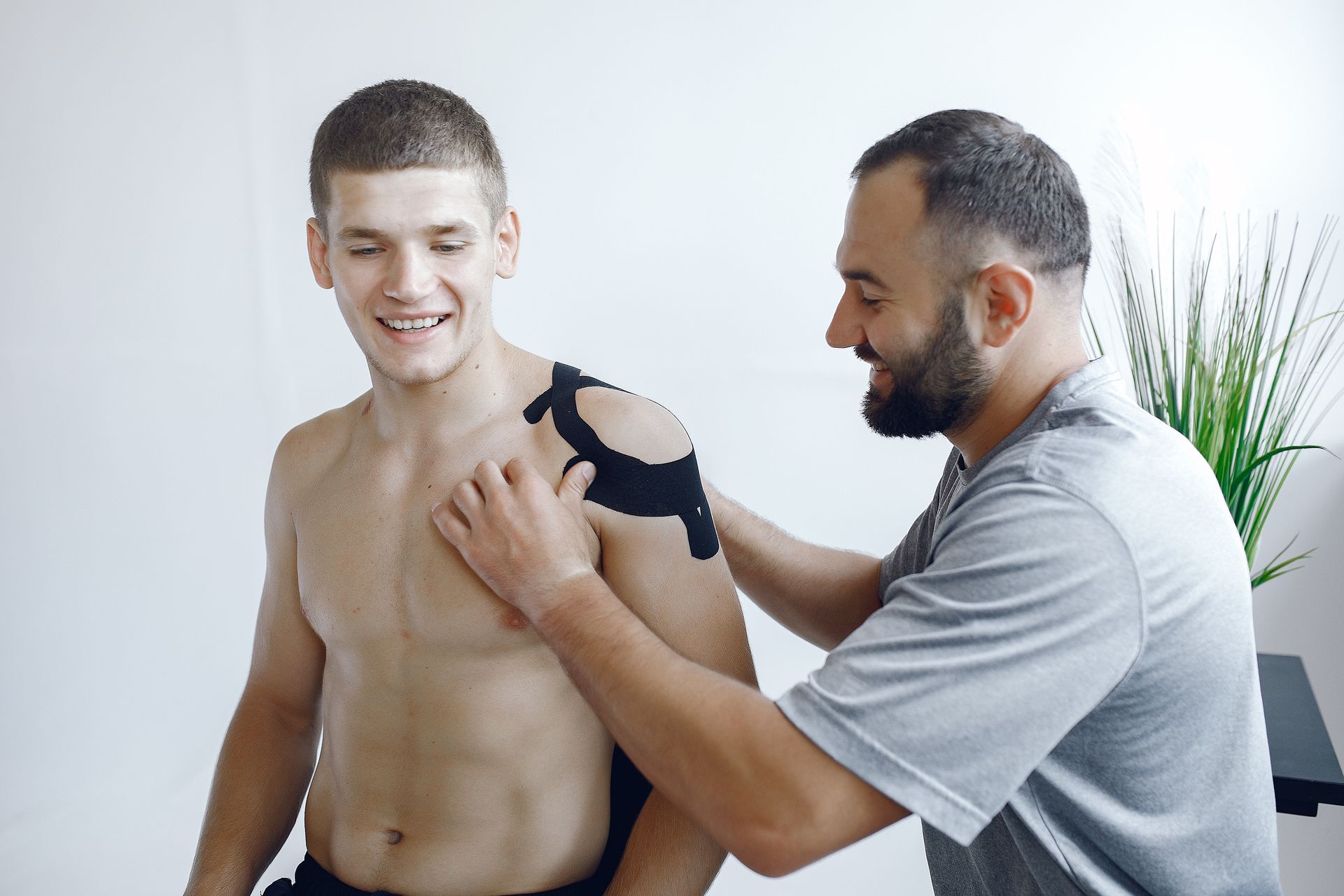 a man is applying kinesio tape to another man 's shoulder .