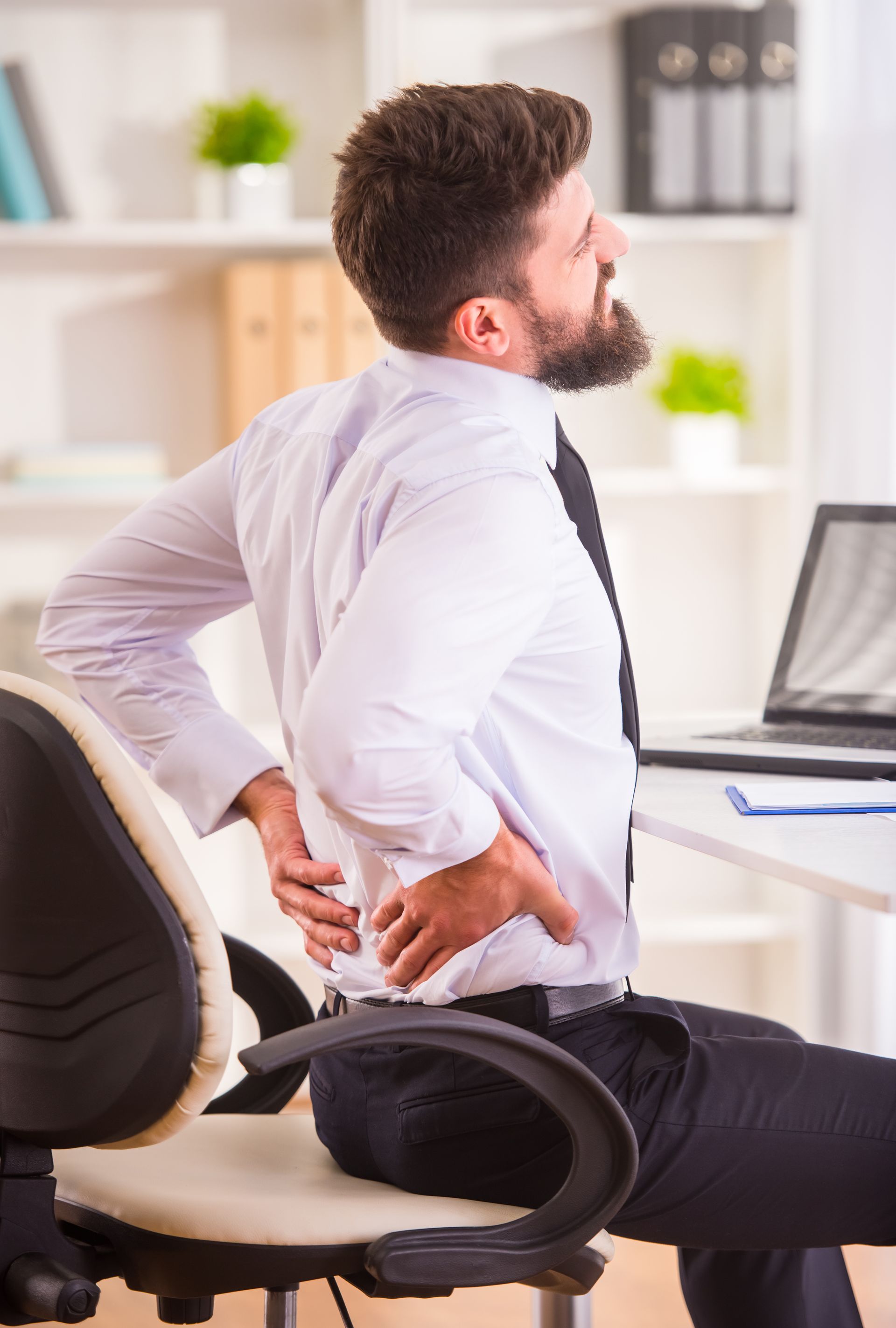 a man is sitting in an office chair holding his back in pain .