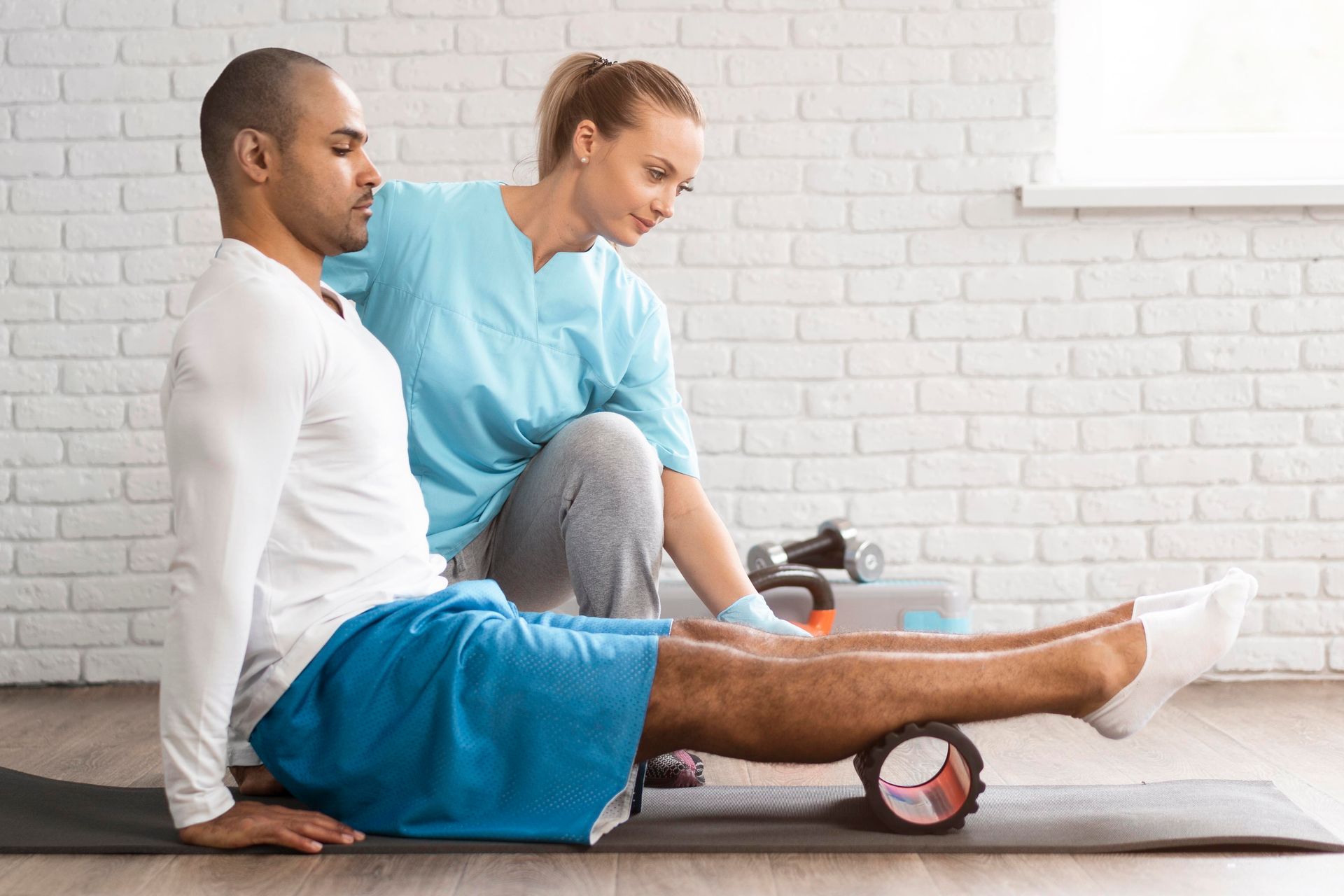 a man is sitting on a yoga mat while a woman rolls his leg with a foam roller .