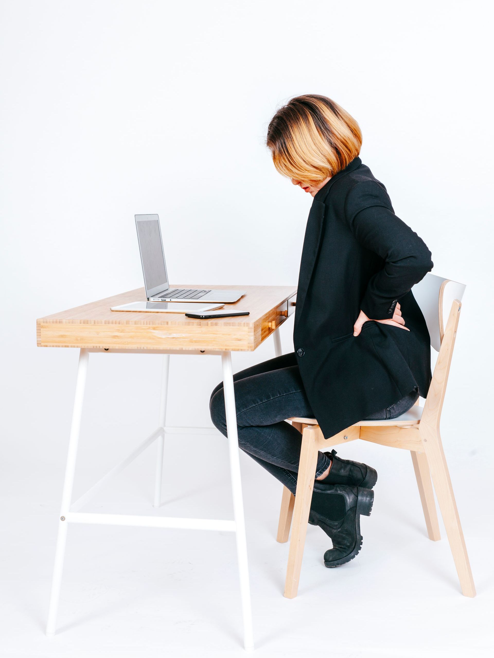 a woman is sitting at a desk with a laptop and has back pain .