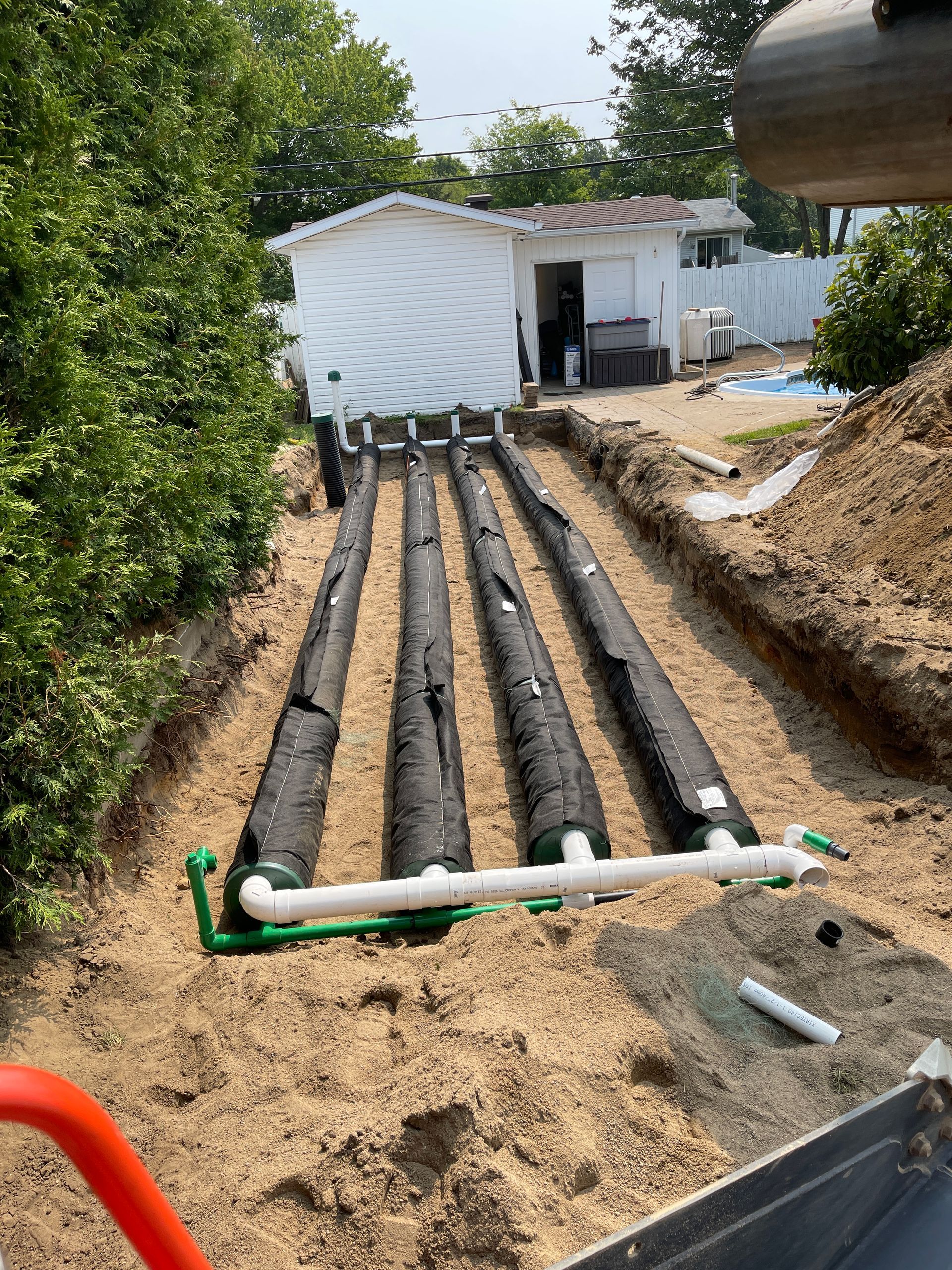 Une rangée de tuyaux est en cours d’installation dans la terre devant une maison.