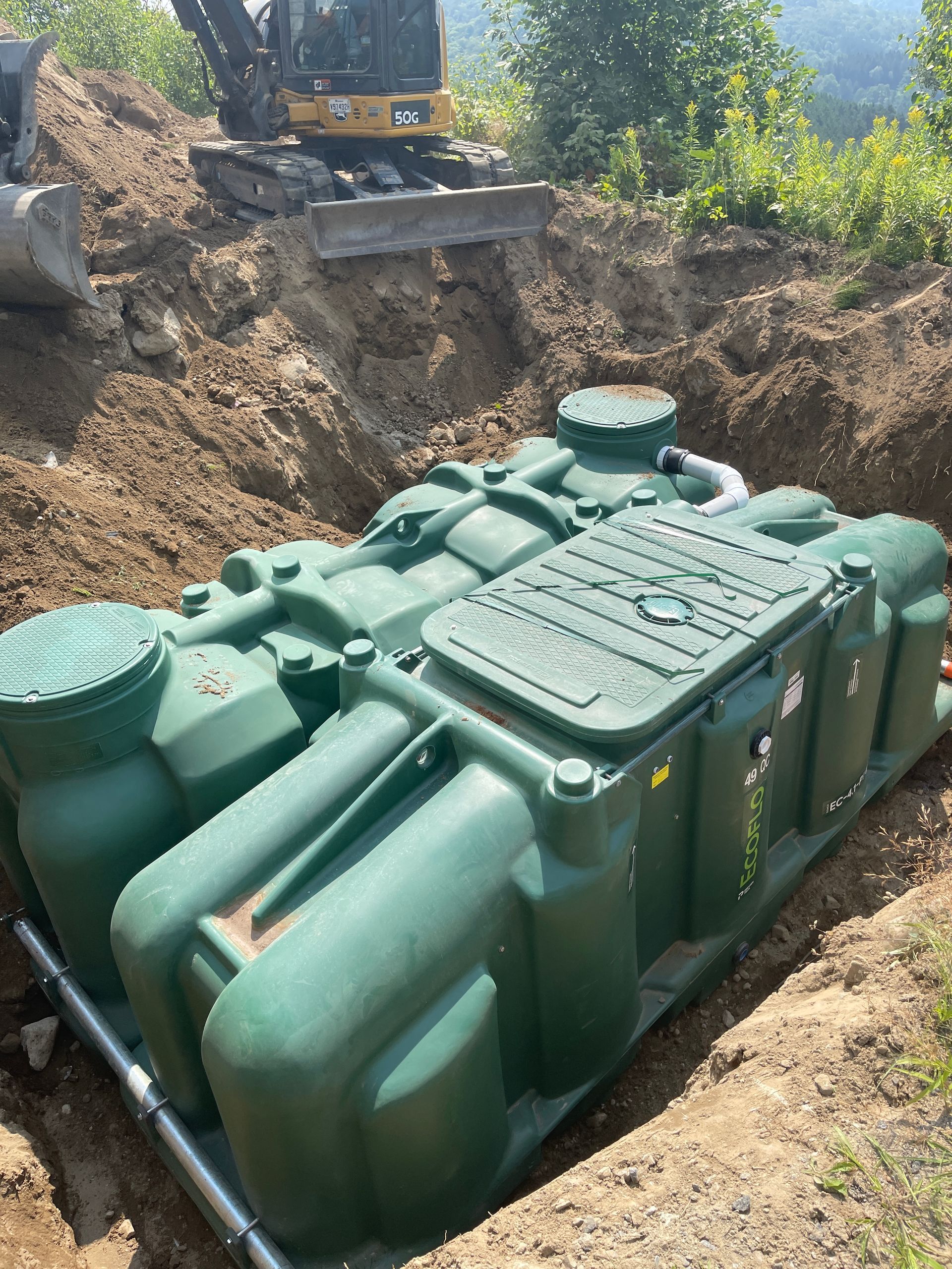 Un grand réservoir vert est posé dans la terre à côté d’un bulldozer.