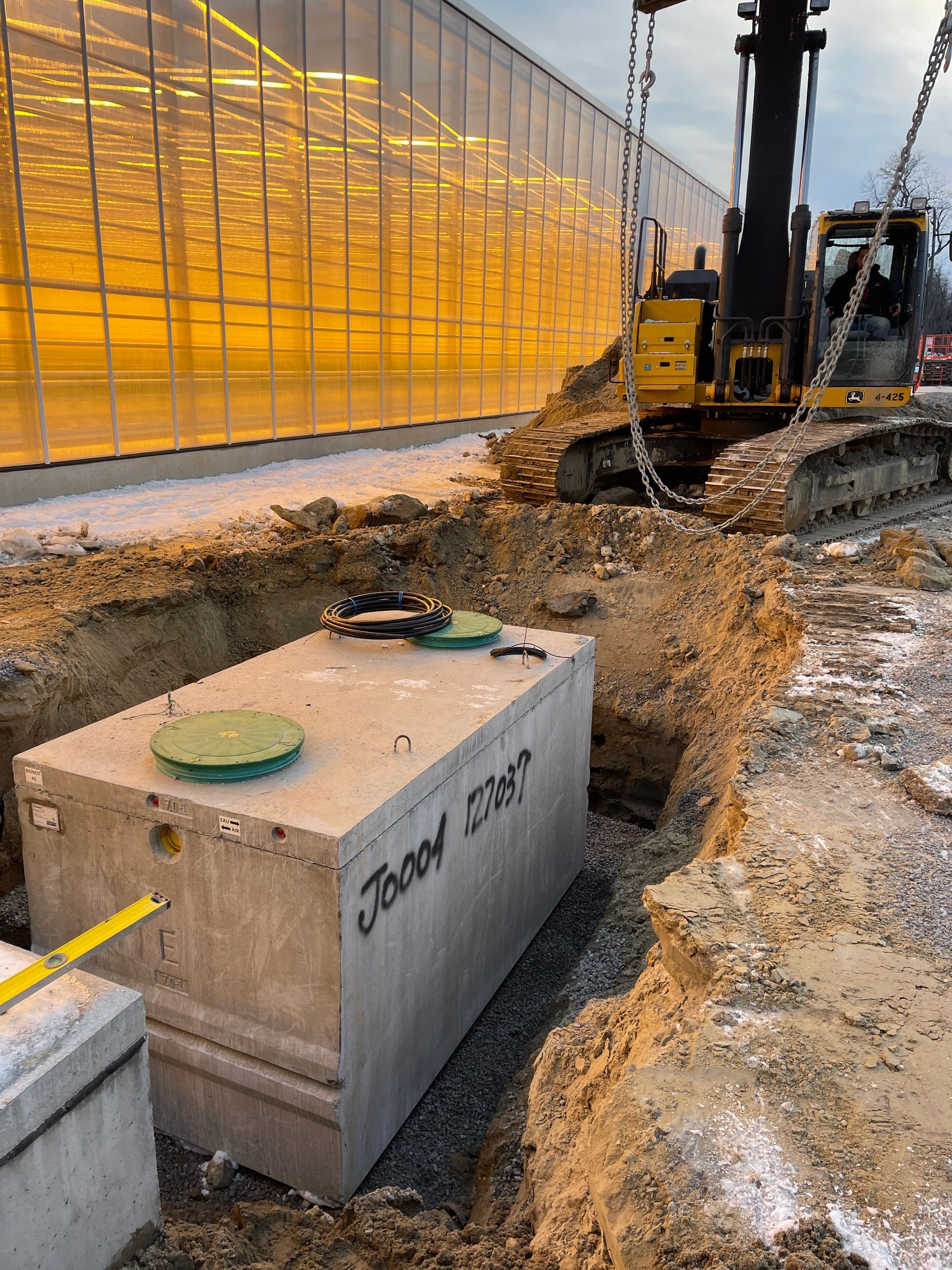 Un gros bloc de béton repose dans la terre devant une serre.