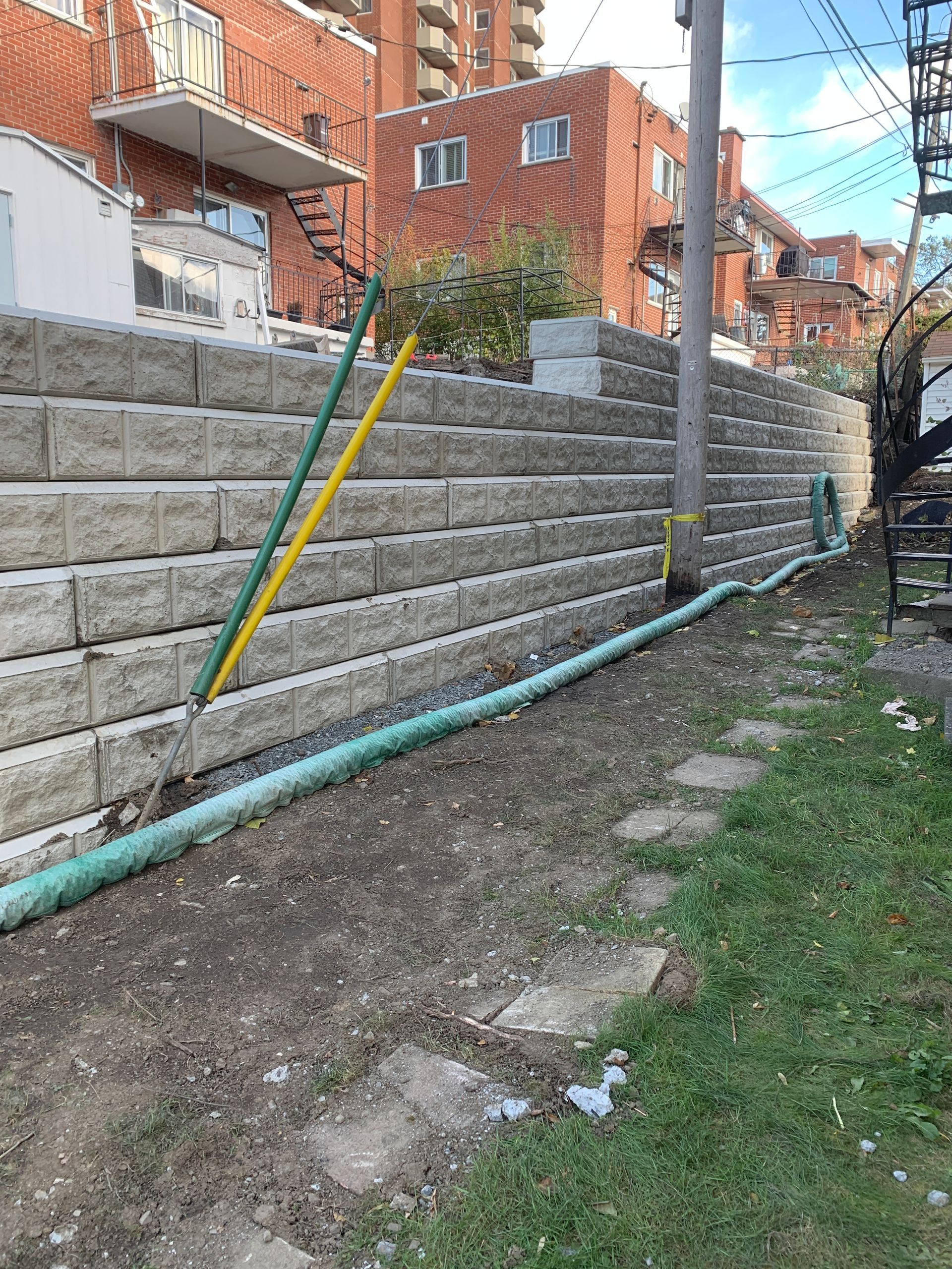 Un mur de briques avec un tuyau vert qui en sort devant un bâtiment en briques.