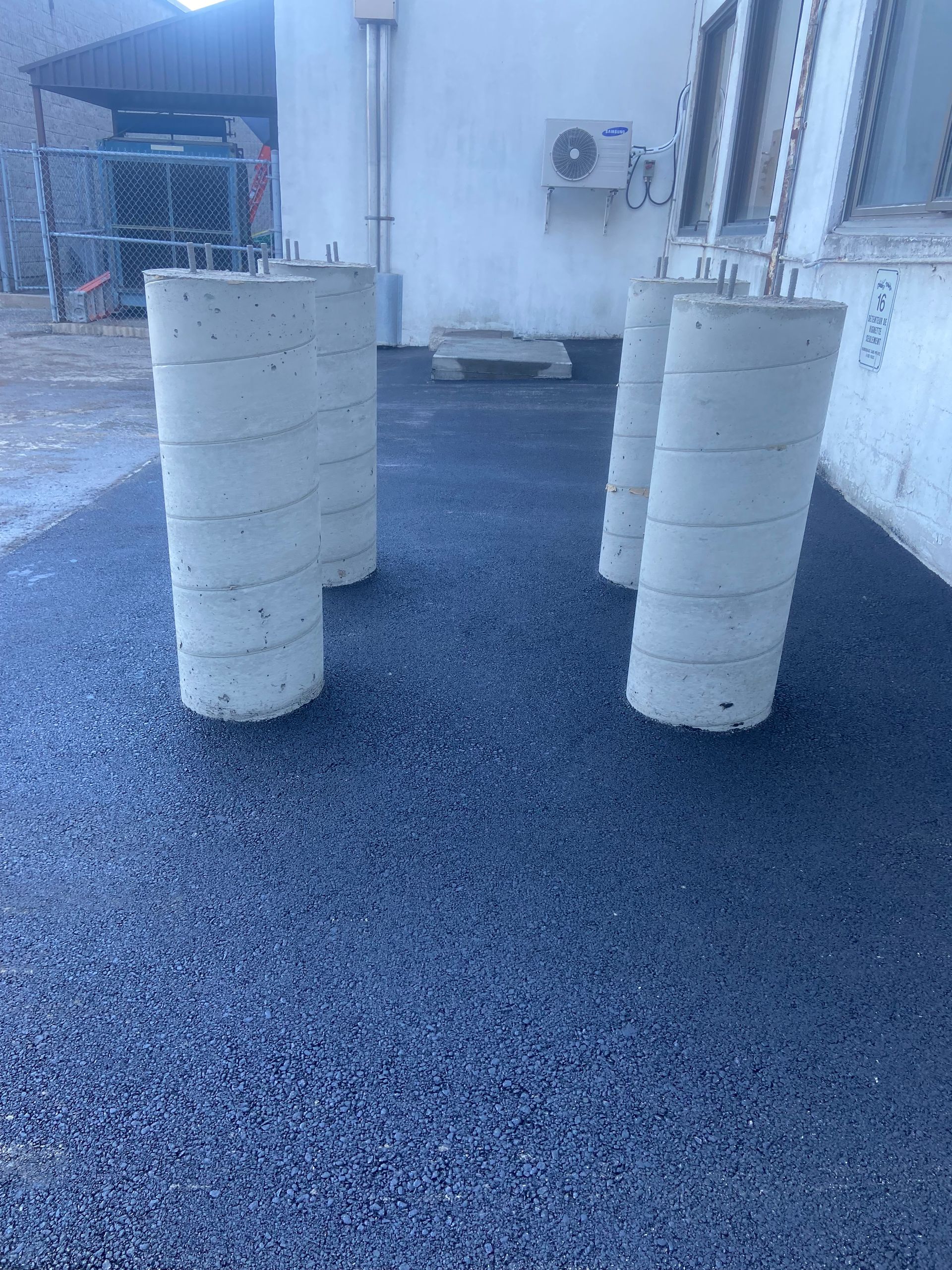 Un groupe de cylindres de béton se trouve au sommet d’une route de gravier.