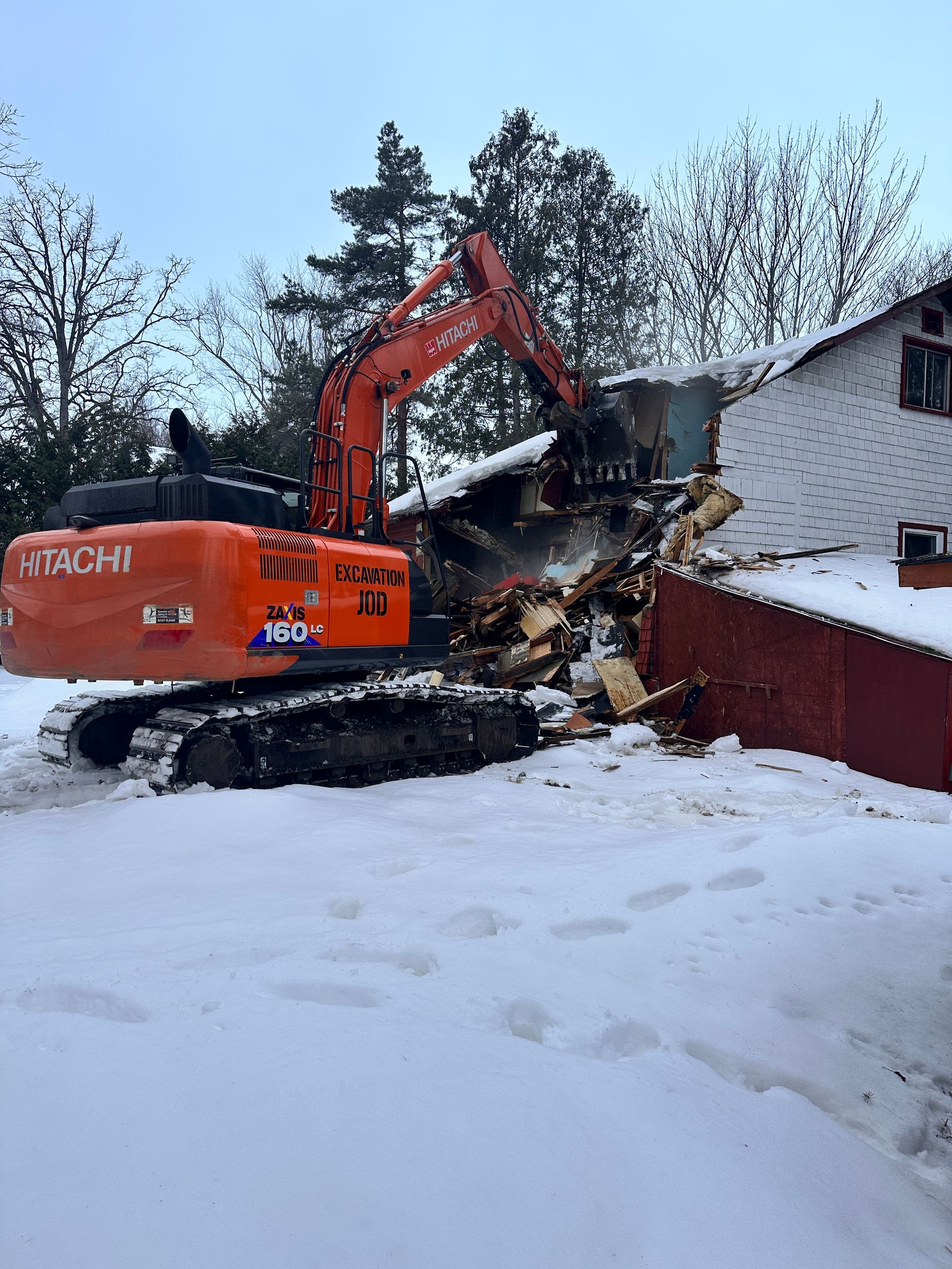 Une excavatrice démolit une maison dans la neige.
