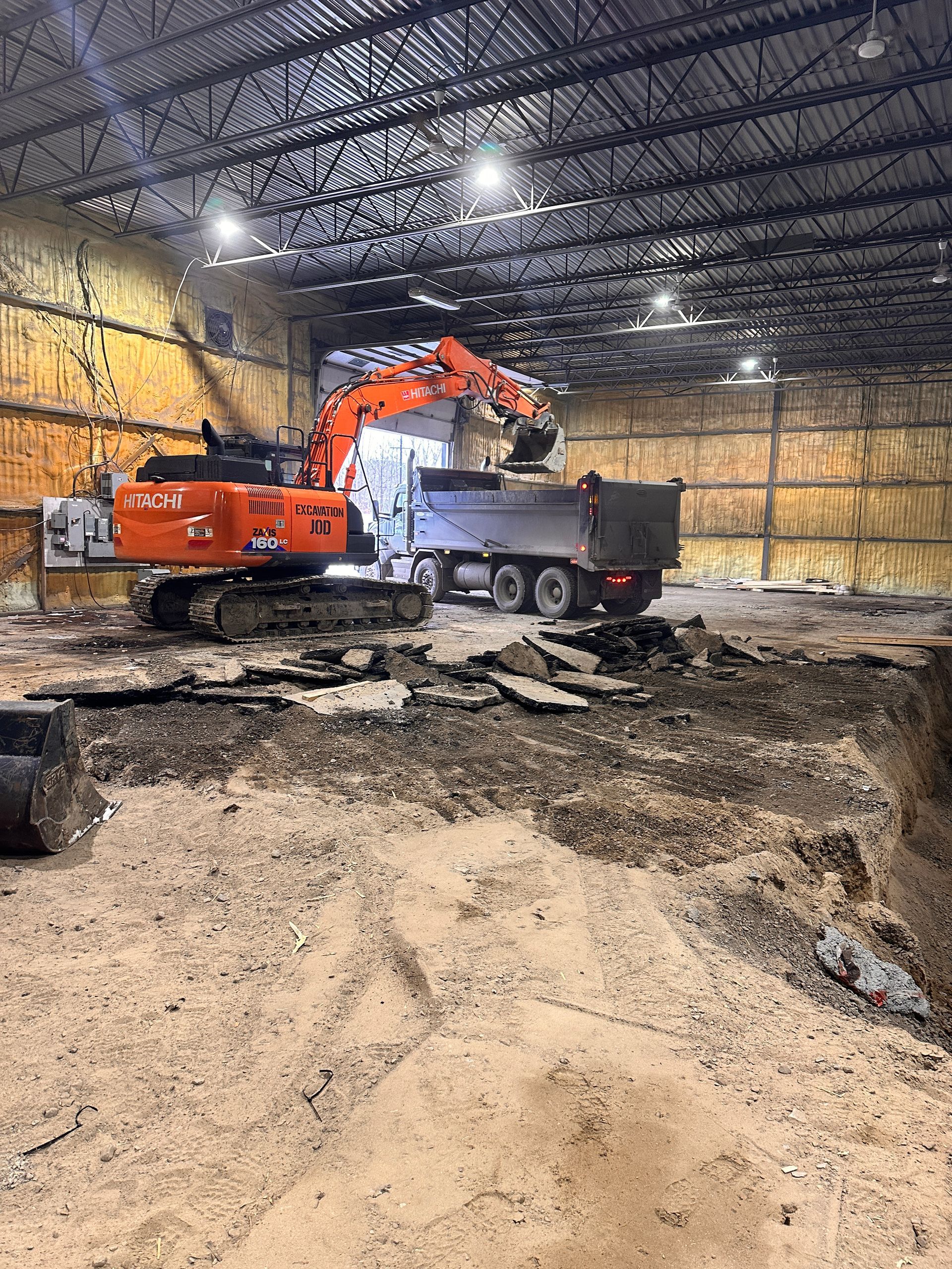 Une excavatrice charge de la terre dans un camion-benne dans un entrepôt.