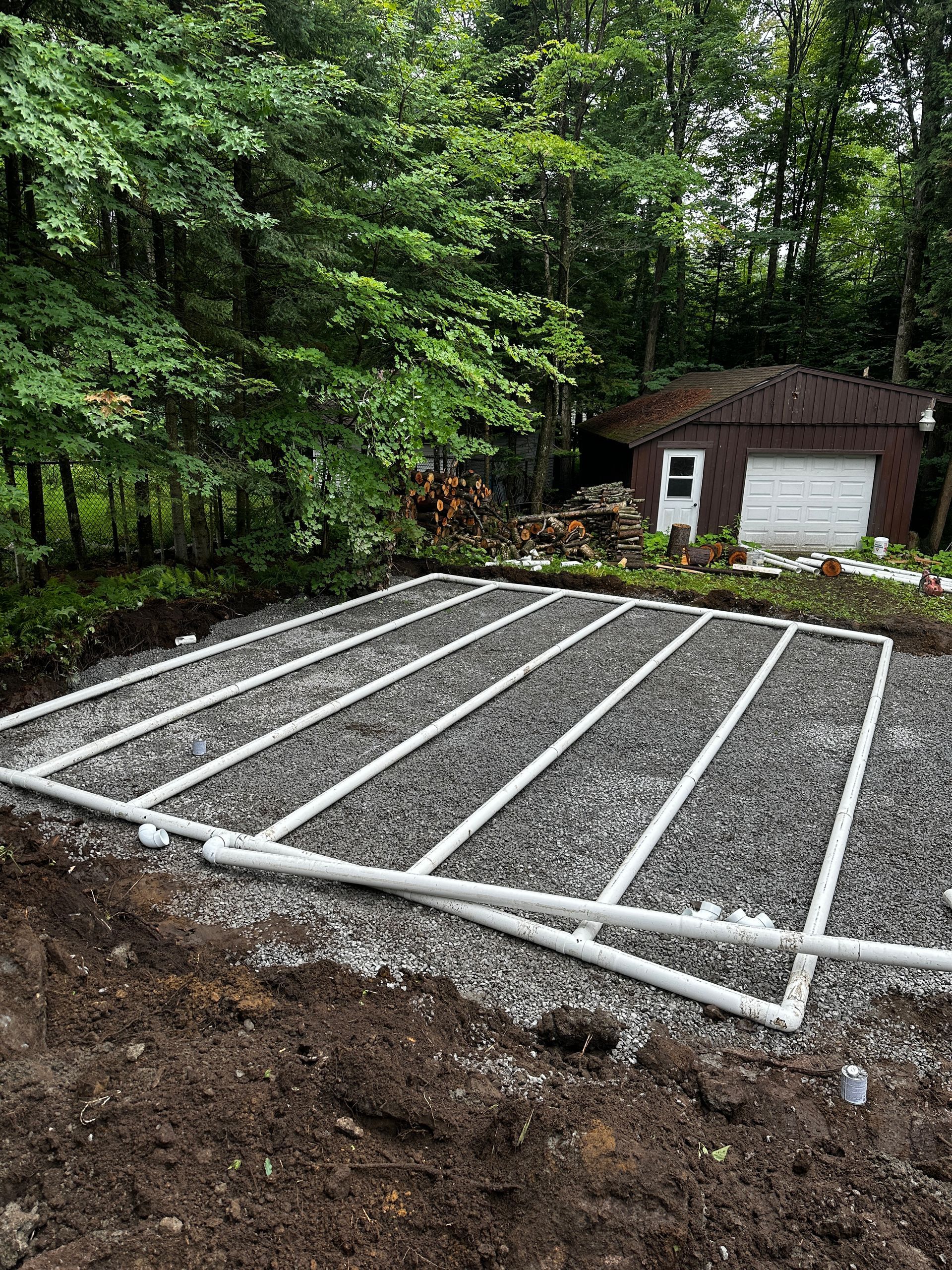 Un système de drainage est en cours d'installation dans une zone de gravier devant un garage.