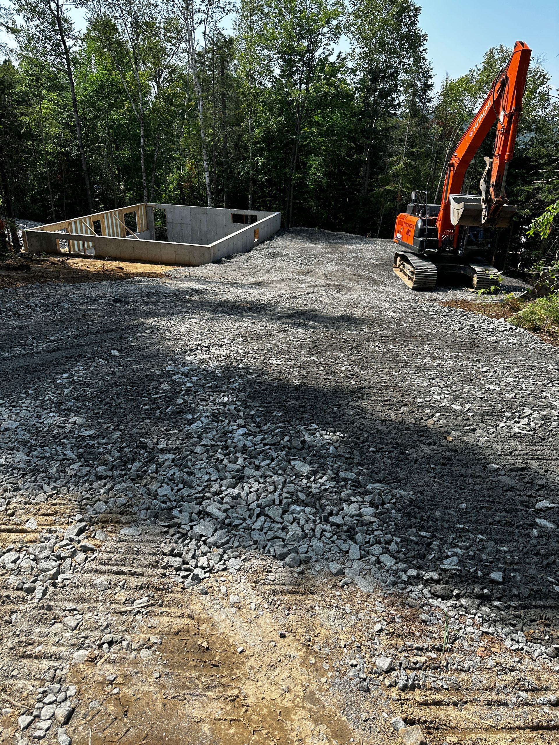 Une grande excavatrice orange se trouve au sommet d’une route de gravier.