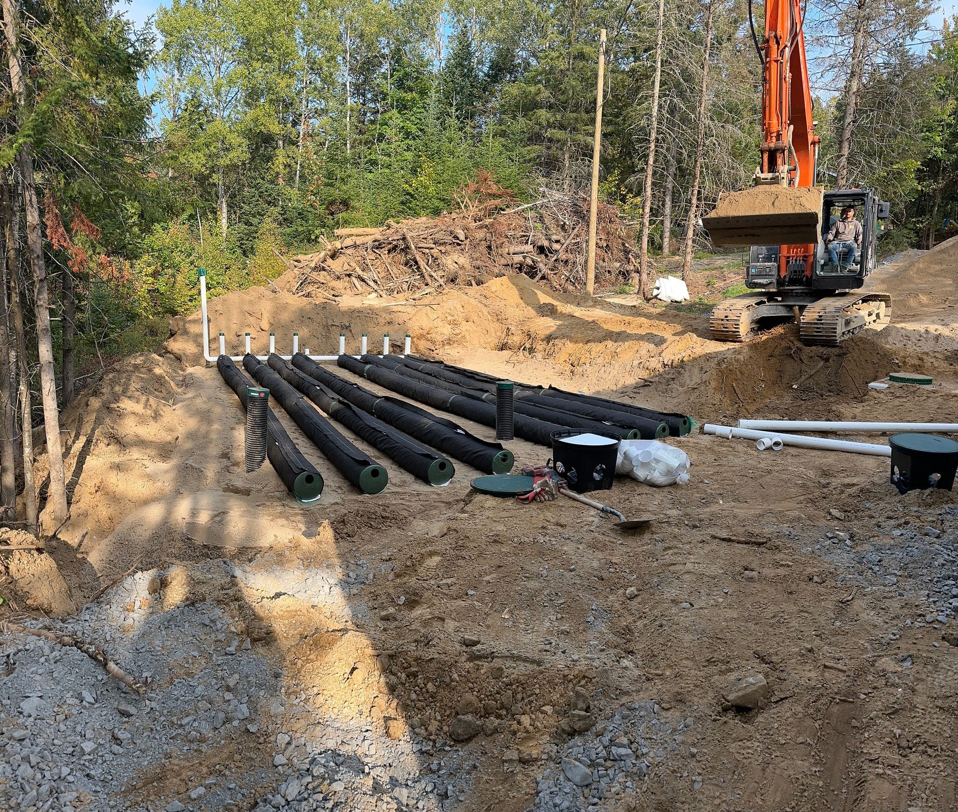 Une excavatrice creuse un trou dans la terre à côté d’un tas de tuyaux.