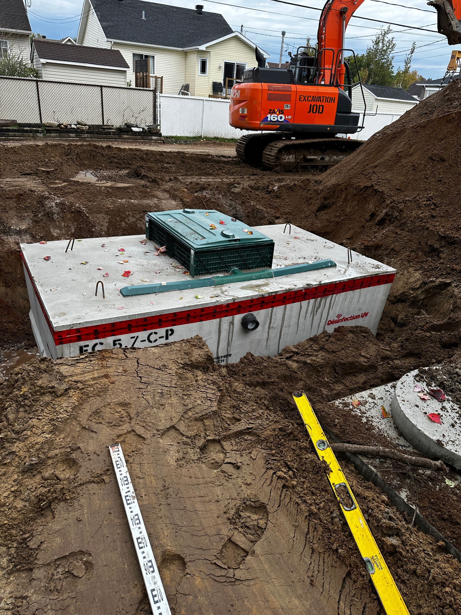 Une grande boîte en béton repose dans la terre à côté d’un niveau jaune.