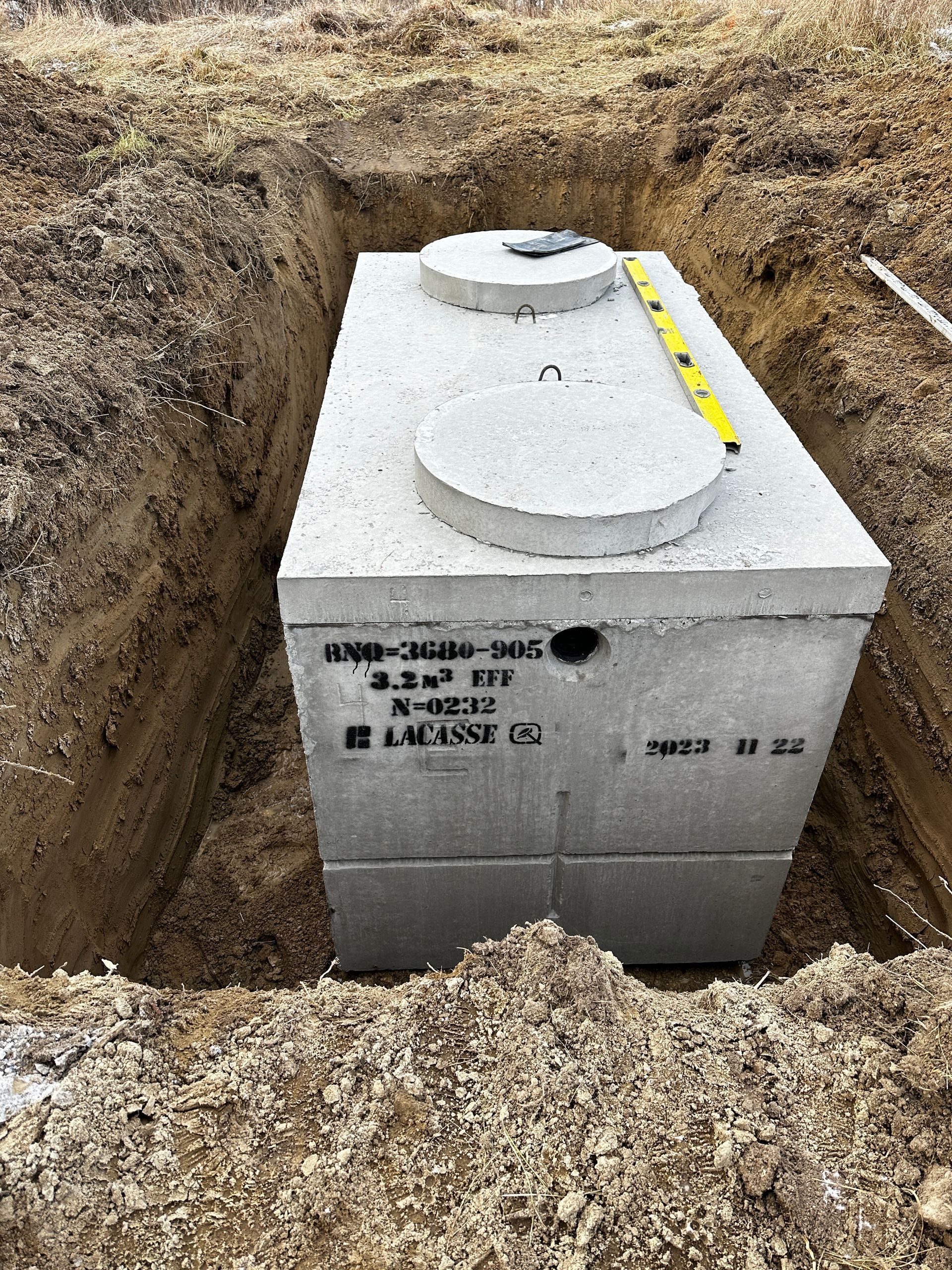 Une grande fosse septique en béton se trouve dans un trou dans le sol.