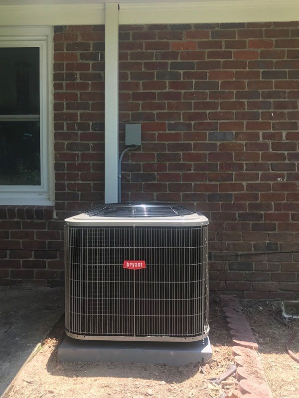 An air conditioner is sitting outside of a brick building next to a window.
