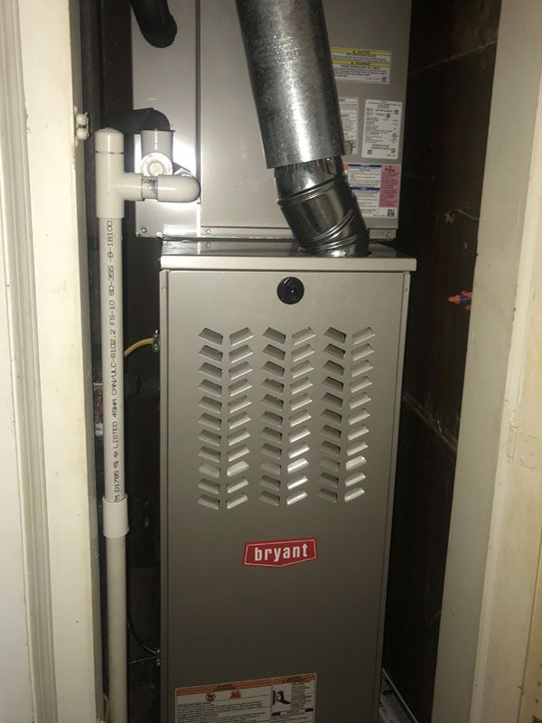 A bryant air conditioner is sitting in a closet next to a door.