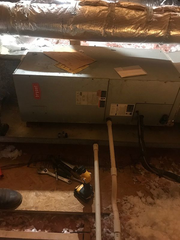 A man is working on an air conditioner in a basement.