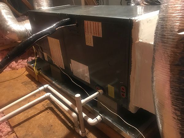 A black air conditioner is sitting on top of a wooden floor in an attic.