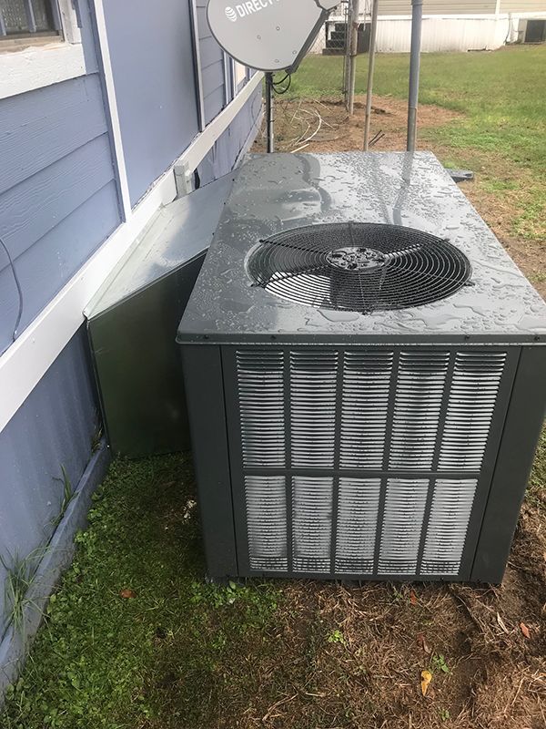 A gray air conditioner is sitting in the grass next to a blue house.