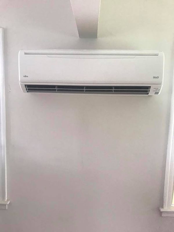 A white air conditioner is hanging on a white wall next to two windows.