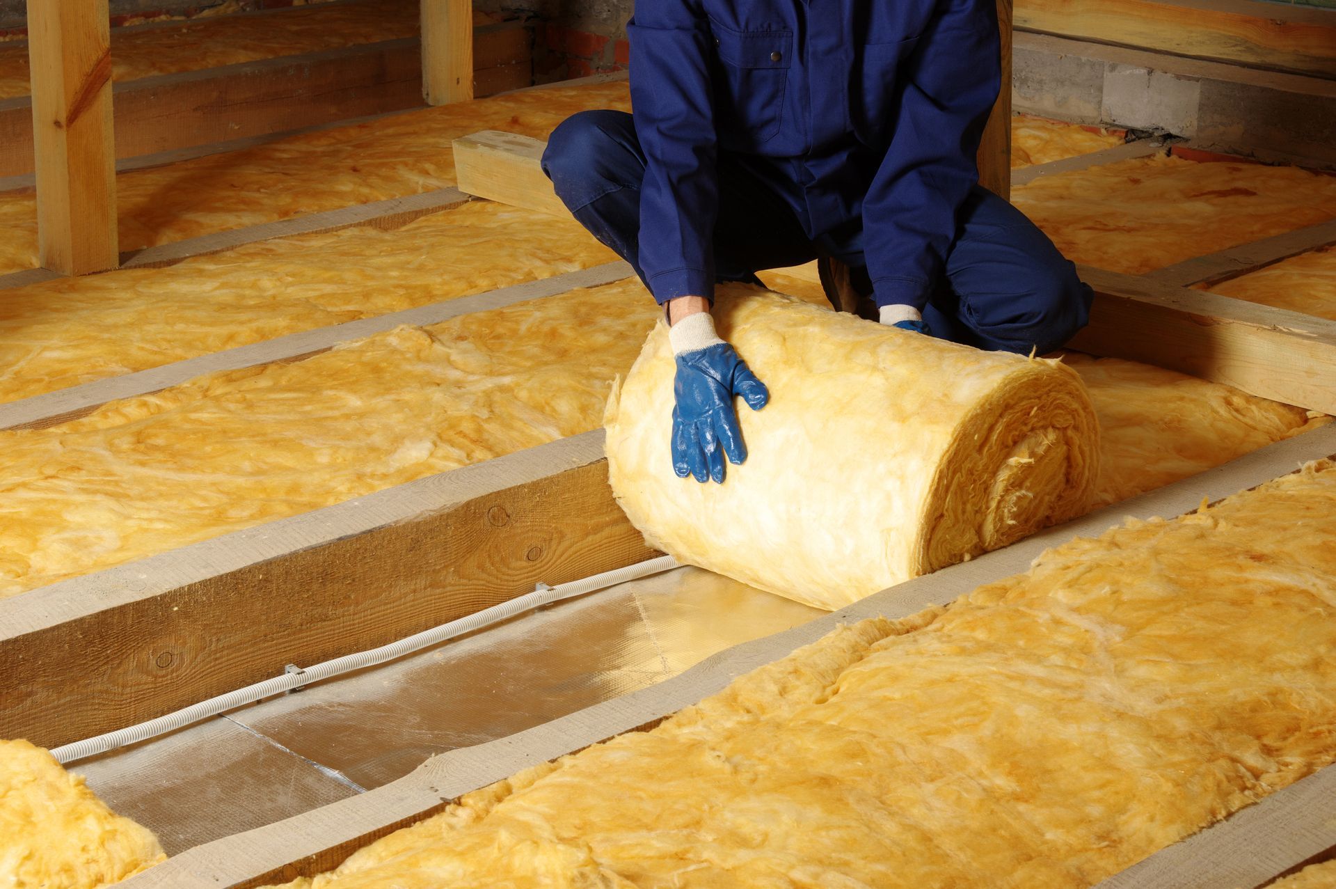 A man is kneeling on the floor holding a roll of insulation.