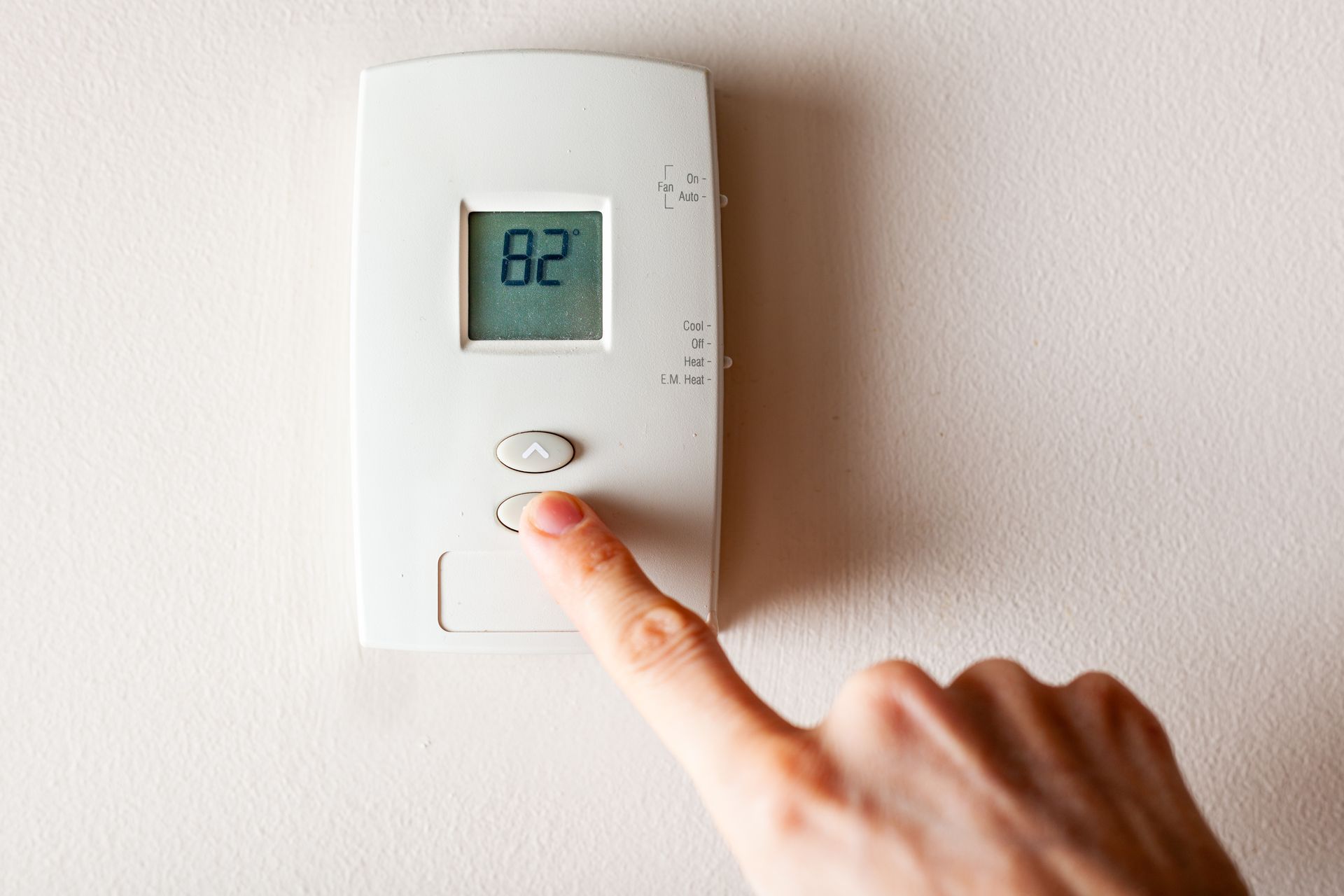 A person is adjusting a thermostat with their finger.