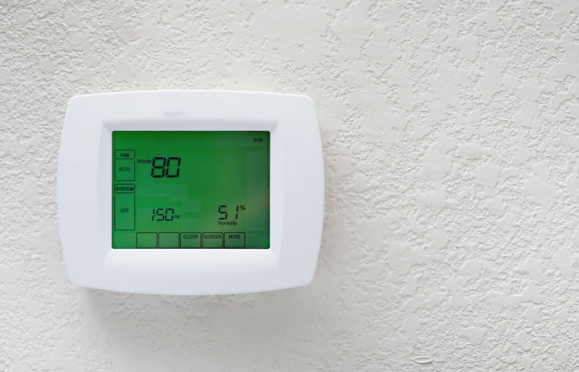 A white thermostat with a green screen is hanging on a white wall.