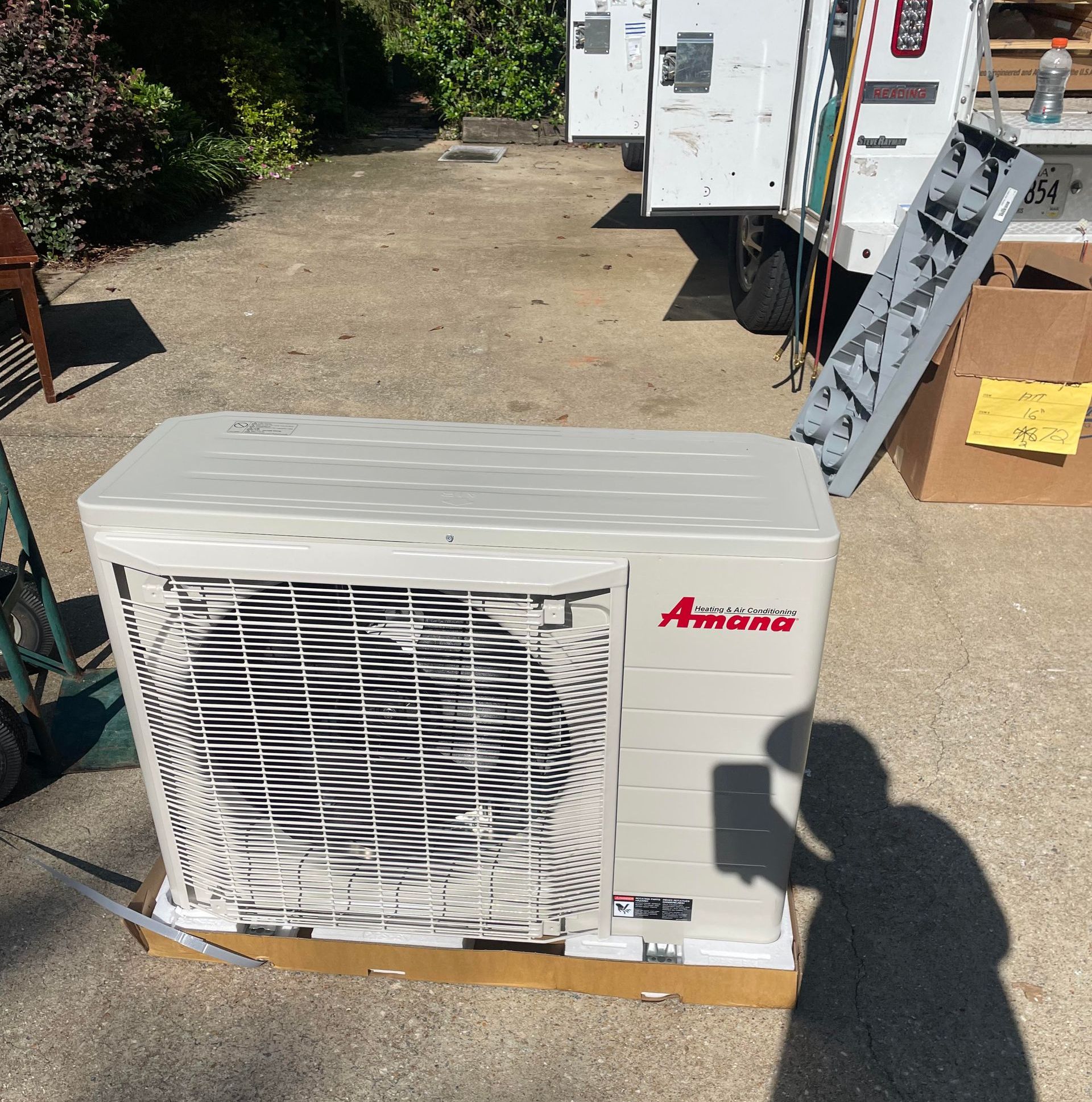 A amana air conditioner is sitting on a box in a driveway