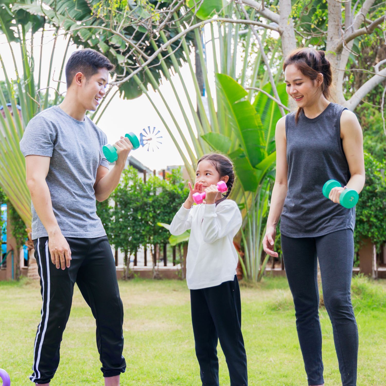 A man , woman and child are holding dumbbells in a park.