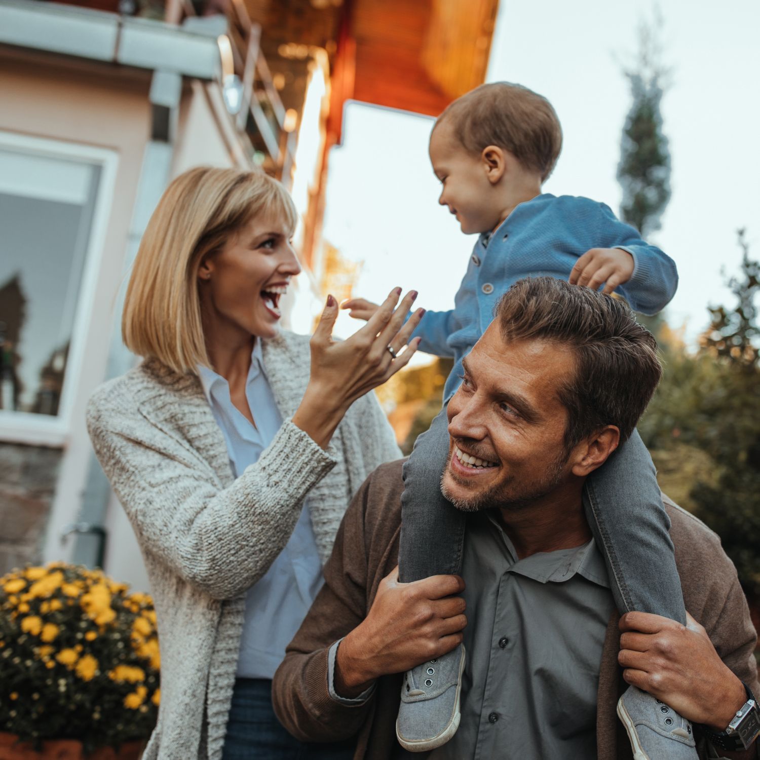 A man is carrying a child on his shoulders while a woman laughs.