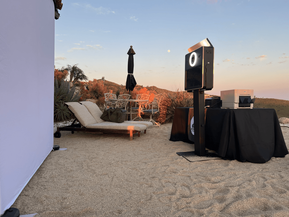 A photo booth is sitting on the beach next to a table and chairs.