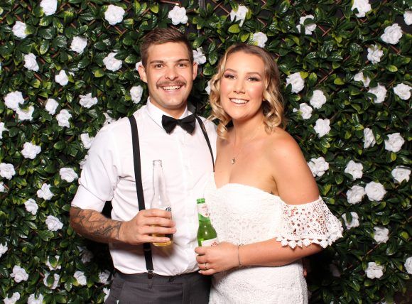A bride and groom are posing for a picture in front of a flower wall.