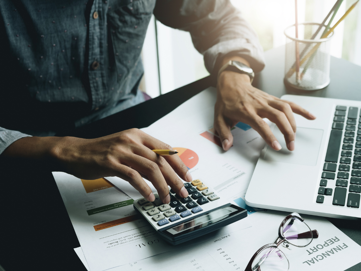 Hands using a calculator beside a laptop and financial charts on a desk
