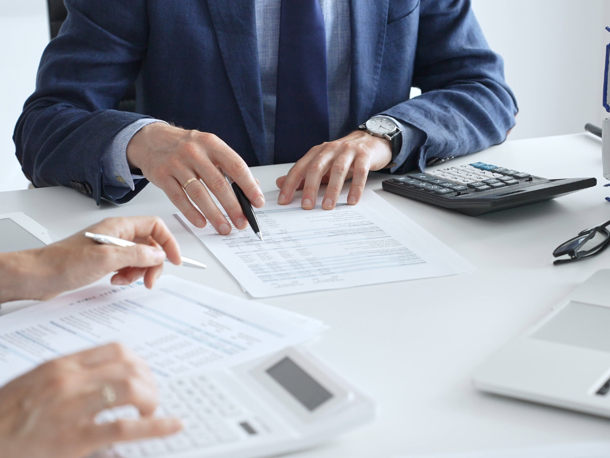 Hands reviewing paperwork at a desk with a calculator and laptop nearby