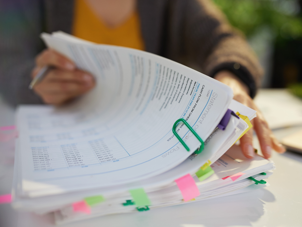 Person holding a stack of annotated documents with colorful tabs and a green paperclip