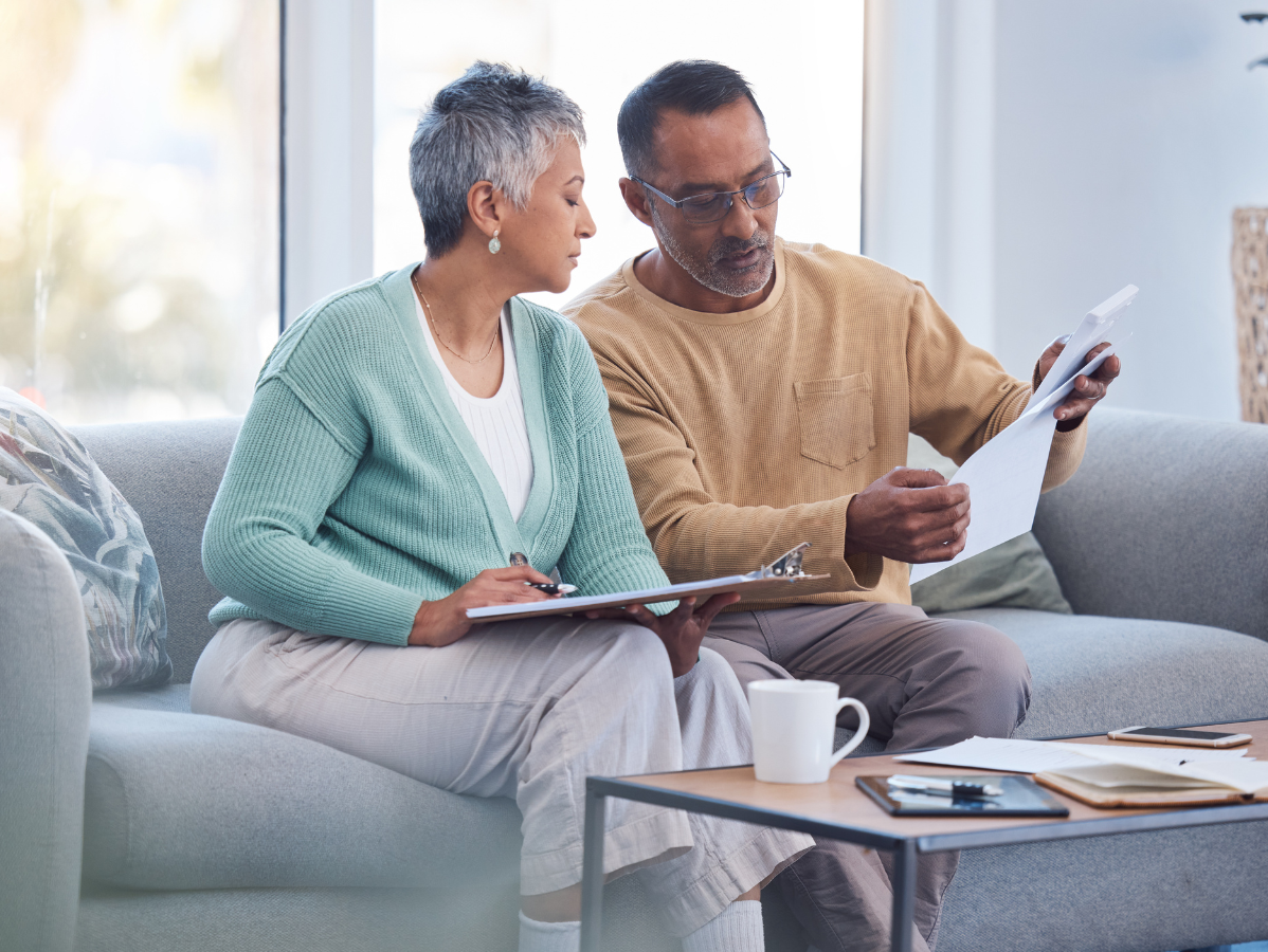 Two people on a sofa reviewing papers in a bright living room with a coffee cup and tablet on the table
