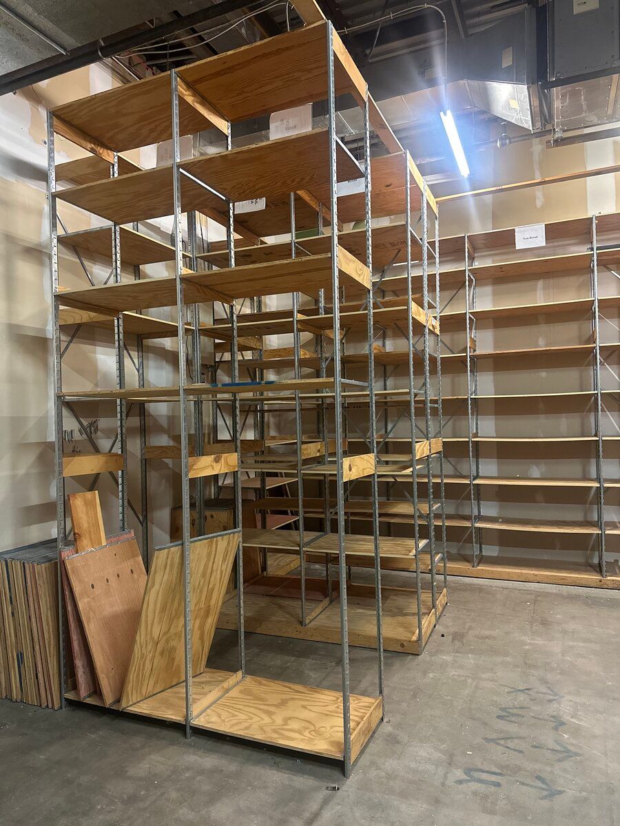 Industrial metal shelving units with wooden boards, standing in a large, empty storage warehouse.