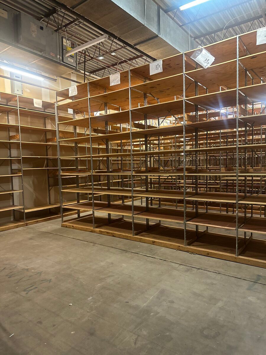 Empty industrial shelving units made of metal, arranged in rows inside a warehouse with a concrete floor.