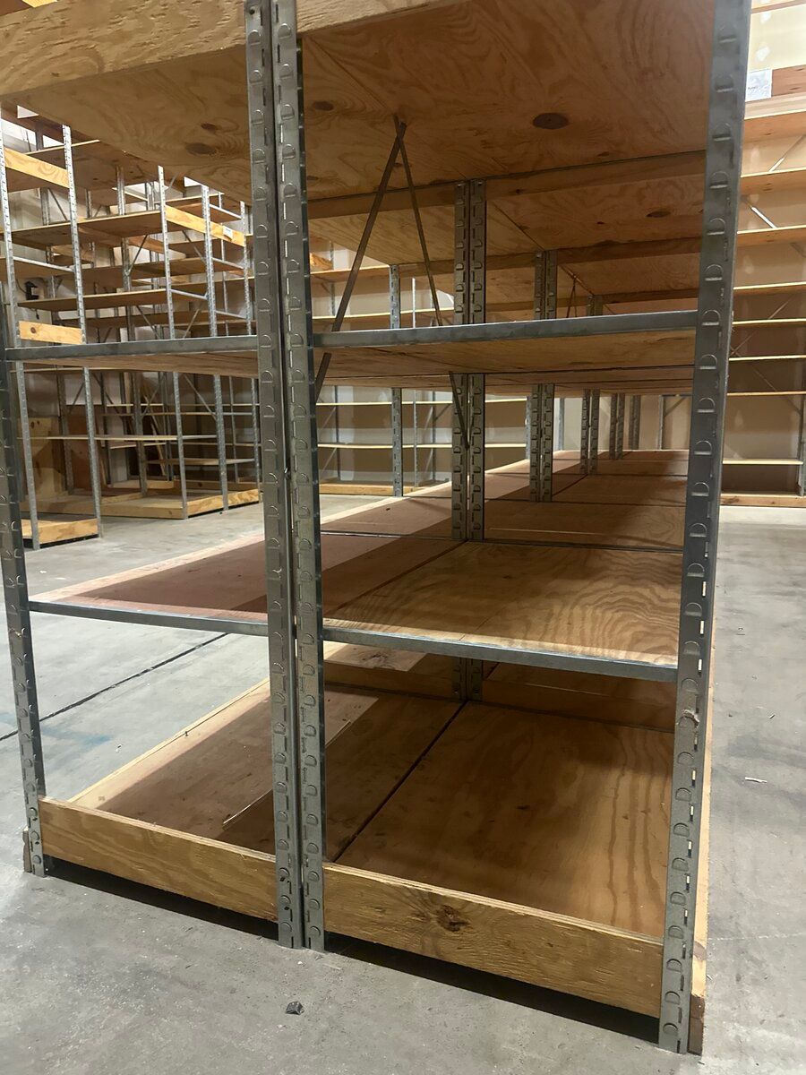 Industrial metal shelving units with wooden plywood shelves in a warehouse setting.