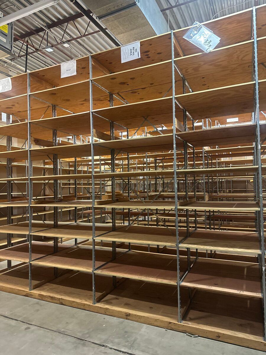 An array of empty, tiered wooden shelves with metal supports inside a warehouse.