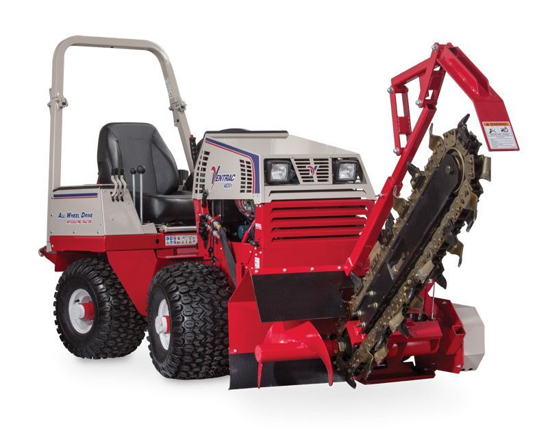 A red and beige Ditch Witch trencher with oversized tires and a large digging chain attachment.